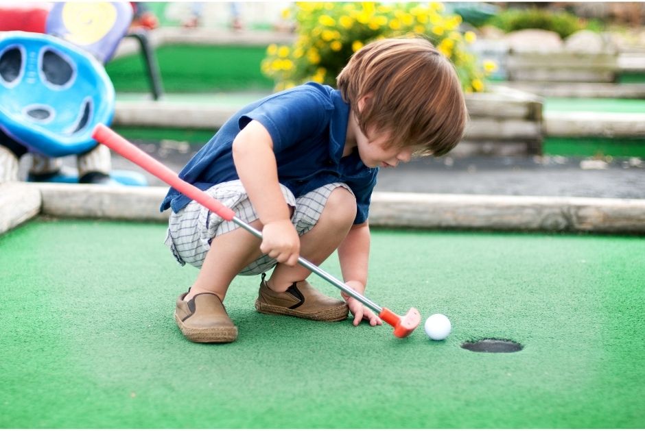 young boy holding a golf club with a ball playing mini-golf