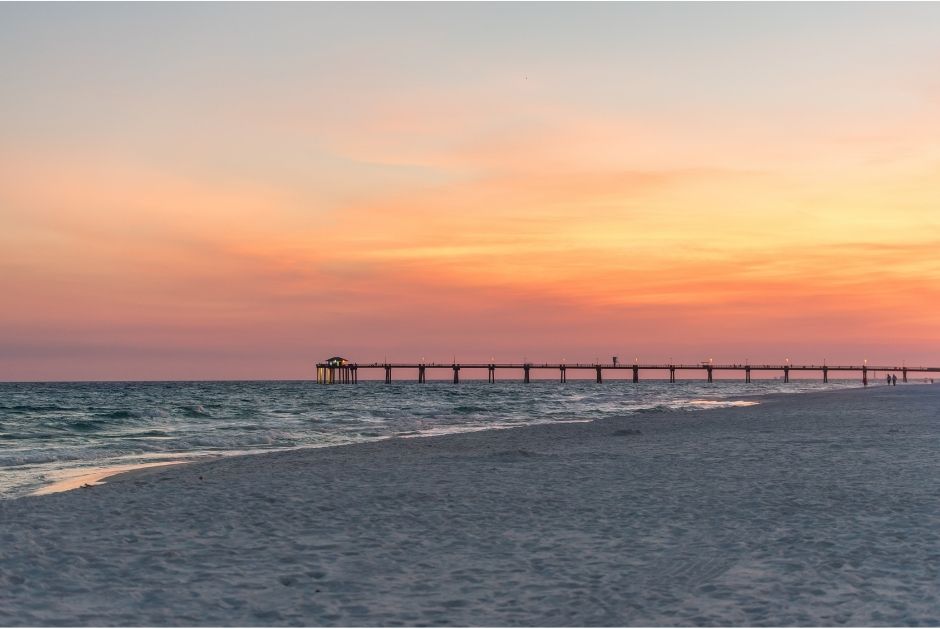 view of the okaloosa island pier with a sunset in the sky and water and sand