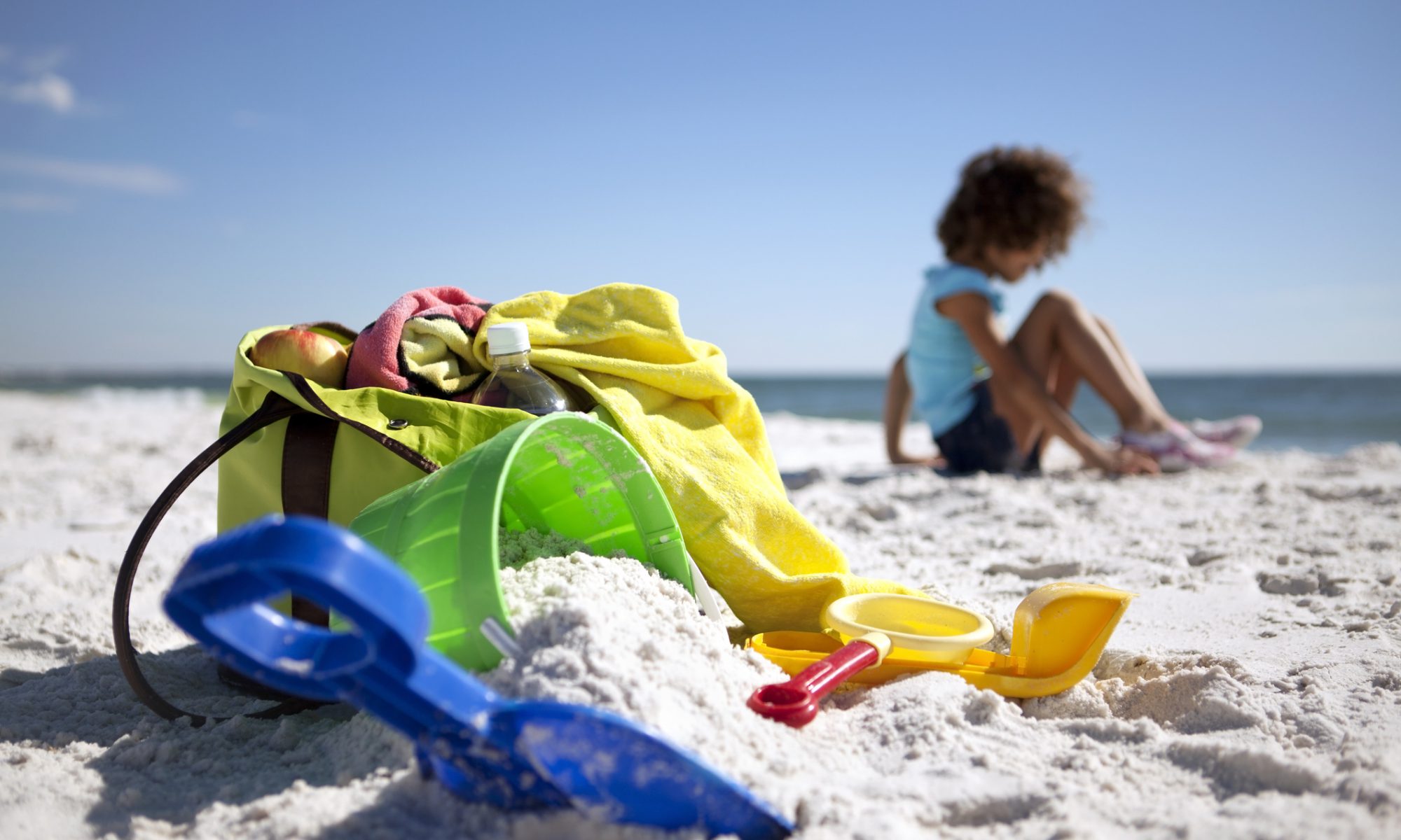 Beach bag, beach toys and a little girl on the beach.